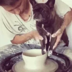 A close-up of a potter's hands at work, holding a dog over a pottery wheel, capturing with humour the essence of artistic expression